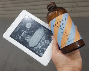 Hand hält Kaffeeflasche und eBookreader mit The Rhyme's Library